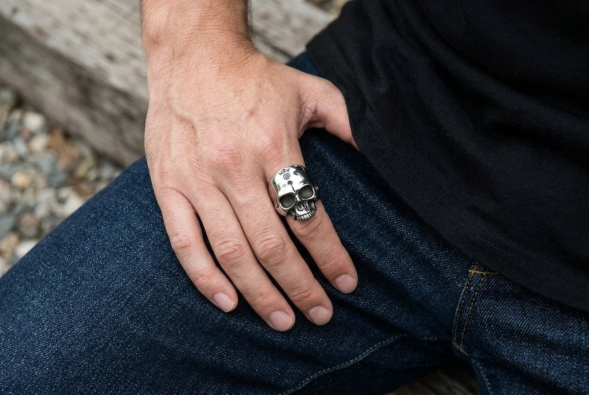 มือสวมแหวนกะโหลก Half Jaw วางบนตักที่สวมยีนส์ข้างเสื้อยืดดำ